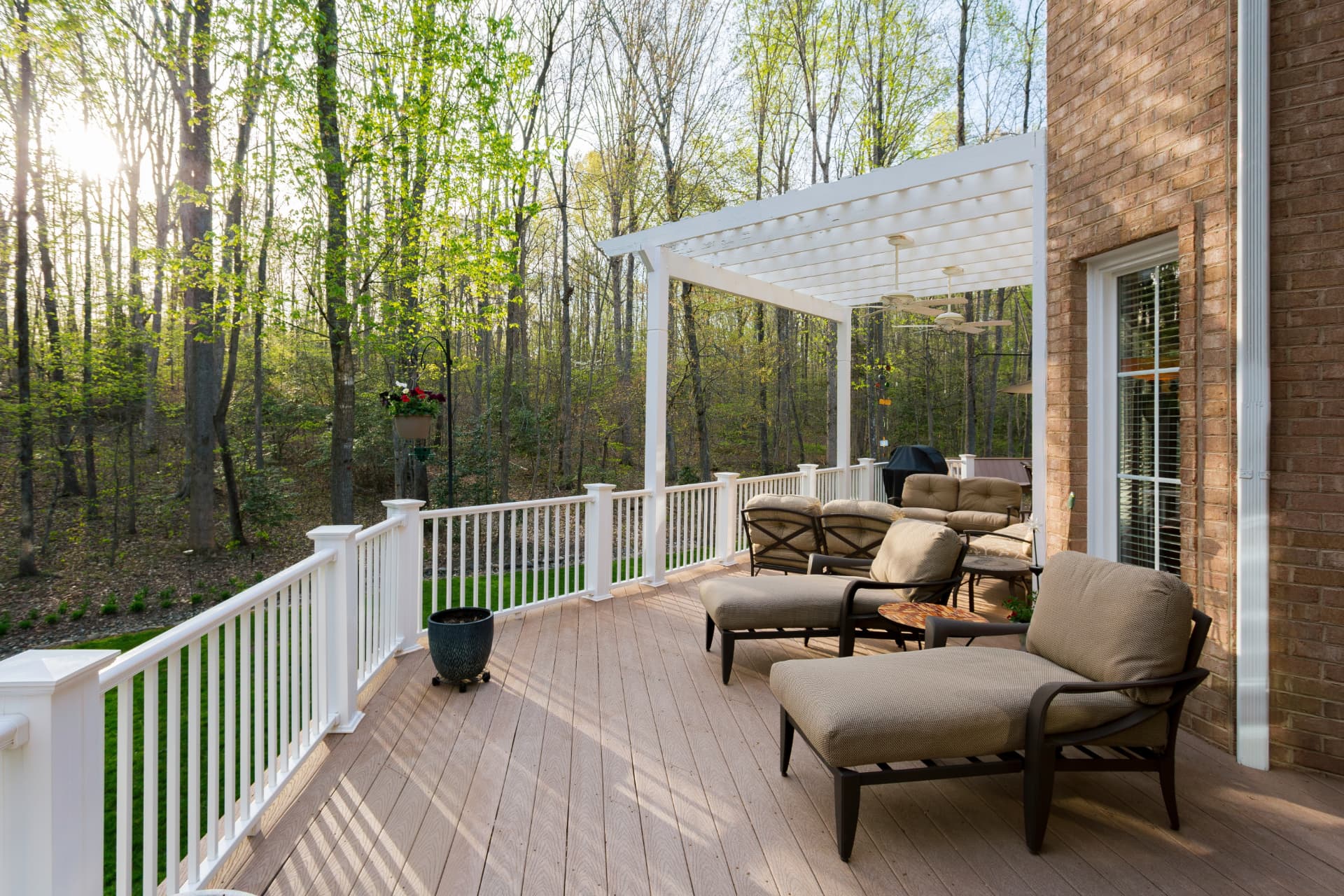 Wood deck with white pergola and railings, outdoor seating, and a wooded backyard view
